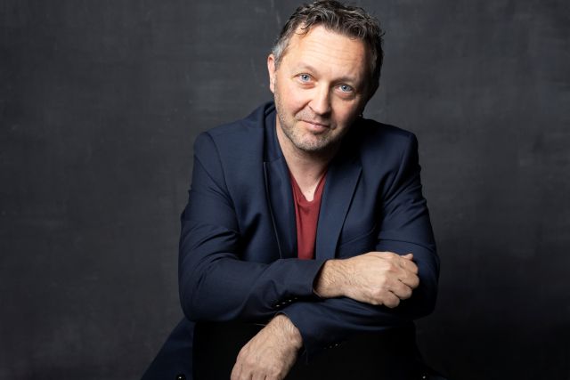 Mies istuu ja katsoo kameraan