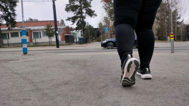 näkökulma maantasalta, etualalla kävelevän ihmisen jalat takaapäin katsottuna, ihminen kävelee kohti suojatietä, jota on juuri ylittämässä auto